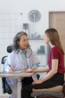 © NanSan - Female elder doctor takes a history of a patient and gives a consultation about osteopathy to a female patient after measuring blood pressure and heart rate and encouragement by holding hands
