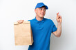 © luismolinero - Young Brazilian man taking a bag of takeaway food isolated on white background with fingers crossing and wishing the best