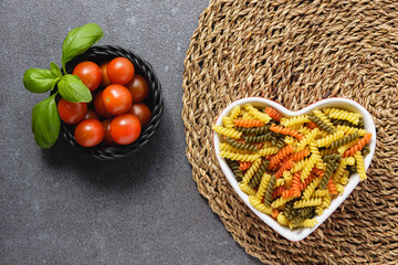 Wall Mural - Raw pasta fusilli in heart bowl with cherry tomatoes and basil.