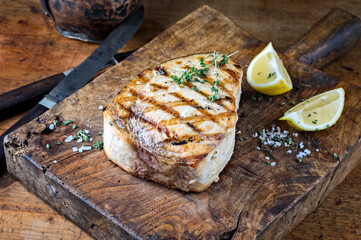 Traditional barbecue swordfish steak with salt and lemon served as close-up on an old rustic wooden board