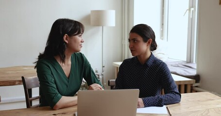 Poster - Confident busy female office coworkers discussing work project, talking, chatting at laptop, sitting at workplace table, speaking, listening, nodding, laughing at joke, collaborating on startup