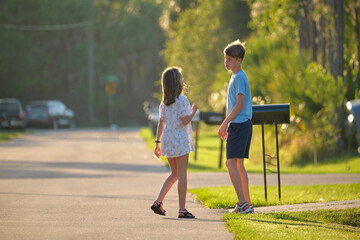  Two young teenage children, girl and boy standing and talking together outdoors on bright sunny day on rural street side