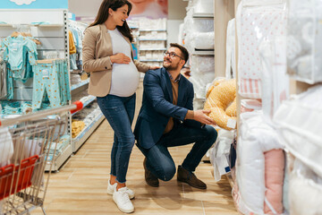 Wall Mural - Attractive middle age couple enjoying in buying clothes and bed sheets for their new baby. Heterosexual couple in baby shop or store. Expecting baby concept.