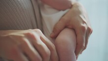 Extreme Close-up Shot Of A Young Mother Holding Her Newborn Baby In Arms And Gently Touching Baby's Knee In Slow-motion