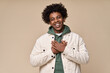 Happy pleased excited grateful African American teen guy holding hands on chest expressing gratitude, feeling trust hope love in heart, impressed with kindness isolated on beige background.