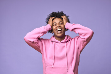 Wall Mural - Young cheerful happy hipster African American teen guy wearing pink hoodie isolated on light purple background. Smiling cool ethnic generation z teenager model laughing standing holding head in hands.