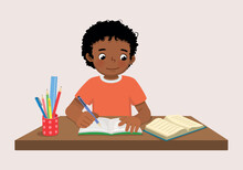 Cute Little African Boy Sitting On The Desk Studying Writing On Notebook Doing His Homework At Home
