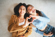 © Monster Ztudio - Top view two happy pretty asian women lying on carpet and posing together hand showing heart shape while looking at the camera