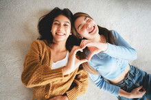Top View Two Happy Pretty Asian Women Lying On Carpet And Posing Together Hand Showing Heart Shape While Looking At The Camera