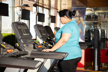 Wall Mural - Young overweight indian woman is workout in gym to lose weight. Asian female doing cardio training and running on treadmill.