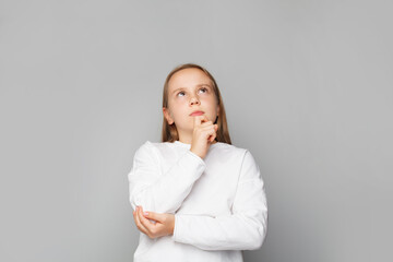 Wall Mural - Serious little girl thinking and looking up on grey background. Idea, brainstorming and education concept