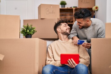 Young couple using touchpad and credit card sitting on sofa at new home