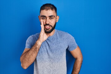 Sticker - Middle east man with beard standing over blue background hand on mouth telling secret rumor, whispering malicious talk conversation