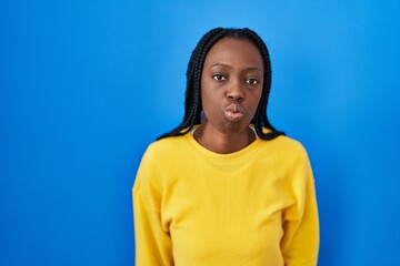 Beautiful black woman standing over blue background looking at the camera blowing a kiss on air being lovely and sexy. love expression.