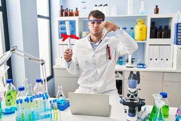 Canvas Print - Young hispanic man working at scientist laboratory holding diploma with angry face, negative sign showing dislike with thumbs down, rejection concept