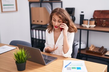 Sticker - Young beautiful hispanic woman business worker talking on smartphone using laptop at office