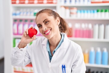 Canvas Print - Young beautiful hispanic woman pharmacist smiling confident holding heart at pharmacy