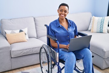 Canvas Print - African american woman using laptop sitting on wheelchair at home