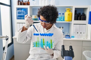 Poster - Young hispanic man wearing scientist uniform using pipette at laboratory