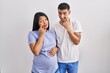 Young hispanic couple expecting a baby standing over background pointing to the eye watching you gesture, suspicious expression