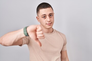 Wall Mural - Young man standing over isolated background looking unhappy and angry showing rejection and negative with thumbs down gesture. bad expression.