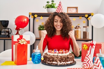 Sticker - Hispanic woman with curly hair celebrating birthday holding big chocolate cake screaming proud, celebrating victory and success very excited with raised arms