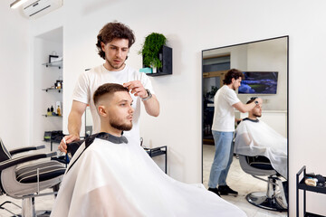 Wall Mural - professional male hairstylist combing young customer's hair