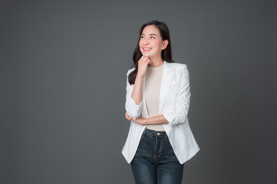 Fototapete - Smiling asian businesswoman standing with arms folded and looking at camera isolated over gray background. Successful 