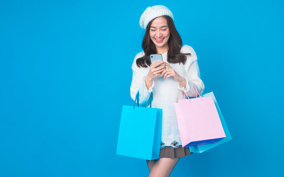 Fototapete - Beautiful young asian woman are holding shopping bags and smartphone with face happily in white seamless on light blue isolated background. Shopping lifestyle. Online shopping concept.