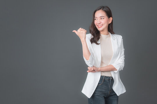 Fototapete - Happy young woman standing isolated over gray background. Looking camera pointing. Cute young woman points a finger away.	