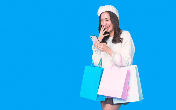 Fototapete - Beautiful young asian woman are holding shopping bags and smartphone with face happily in white seamless on light blue isolated background. Shopping lifestyle. Online shopping concept.