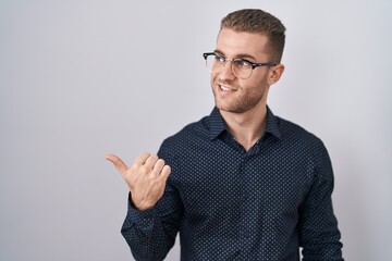 Sticker - Young caucasian man standing over isolated background smiling with happy face looking and pointing to the side with thumb up.