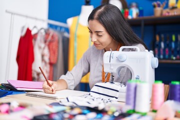 Canvas Print - Young beautiful hispanic woman tailor smiling confident drawing on notebook at clothing factory