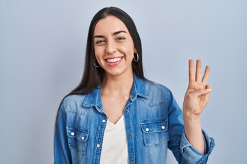 Canvas Print - Hispanic woman standing over blue background showing and pointing up with fingers number three while smiling confident and happy.