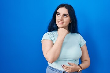 Sticker - Young modern girl with blue hair standing over blue background with hand on chin thinking about question, pensive expression. smiling and thoughtful face. doubt concept.