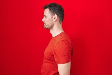 Poster - Young hispanic man standing over red background looking to side, relax profile pose with natural face and confident smile.