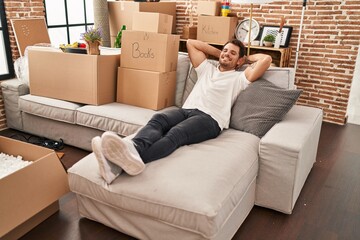 Poster - Young hispanic man relaxed with hands on head sitting on sofa at new home