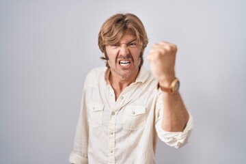 Sticker - Middle age man standing over isolated background angry and mad raising fist frustrated and furious while shouting with anger. rage and aggressive concept.