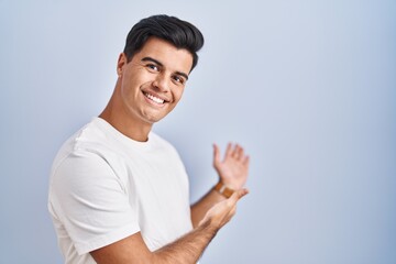 Poster - Hispanic man standing over blue background inviting to enter smiling natural with open hand