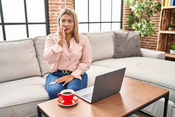 Poster - Young hispanic woman using laptop sitting on the sofa at home looking stressed and nervous with hands on mouth biting nails. anxiety problem.