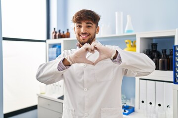 Wall Mural - Arab man with beard working at scientist laboratory smiling in love doing heart symbol shape with hands. romantic concept.