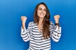 © Krakenimages.com - Young hispanic woman standing over blue isolated background celebrating surprised and amazed for success with arms raised and eyes closed. winner concept.