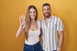 © Krakenimages.com - Young couple standing over yellow background showing and pointing up with fingers number four while smiling confident and happy.