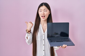 Poster - Chinese young woman holding laptop showing screen pointing thumb up to the side smiling happy with open mouth