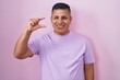© Krakenimages.com - Young hispanic man standing over pink background smiling and confident gesturing with hand doing small size sign with fingers looking and the camera. measure concept.