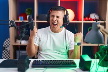 Sticker - Young hispanic man playing video games very happy and excited doing winner gesture with arms raised, smiling and screaming for success. celebration concept.