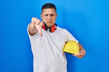 Canvas Print - Hispanic young man holding hardhat with angry face, negative sign showing dislike with thumbs down, rejection concept