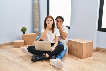 Poster - Young couple using laptop at new home shocked covering mouth with hands for mistake. secret concept.