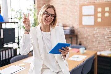 Canvas Print - Young caucasian woman working at the office wearing glasses smiling with happy face winking at the camera doing victory sign with fingers. number two.