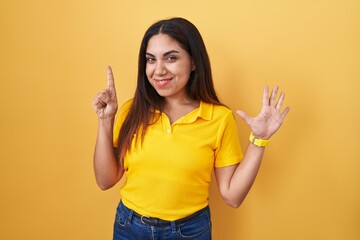 Wall Mural - Young arab woman standing over yellow background showing and pointing up with fingers number six while smiling confident and happy.